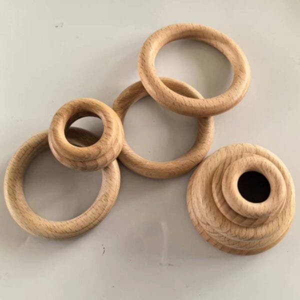 Five beech wood circles of varying sizes, with one ring stacked on a wooden base, are arranged on a plain, light-colored surface—ideal as curtain rings or for creative projects from a trusted manufacturer.