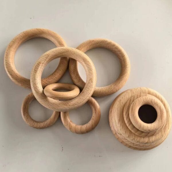 Seven beech wood circles of varying sizes are arranged on a light surface, resembling curtain rings—five lying flat and two stacked for a DIY custom sizes display.