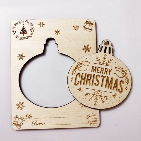 A wooden card with a pop-out ornament reading "Merry Christmas 2021," featuring festive engravings and spaces for "To" and "From"—a perfect eco-friendly wood craft piece for tree wish cards.
