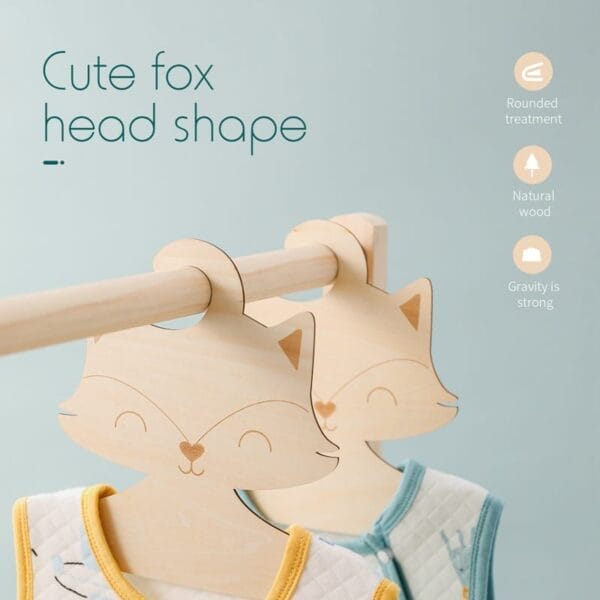 Two adorable wood hangers, shaped like fox faces, hold children’s garments on a wooden rod; accompanying text highlights their charming features.