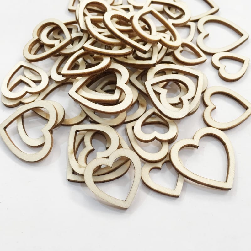 A pile of thin, laser-cut wood heart shapes, some solid and some with hollow centers, scattered on a white surface.