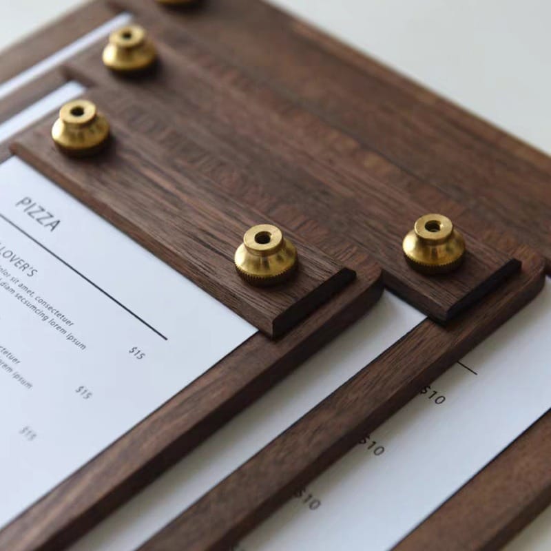 Close-up of elegant black walnut wood menu holders with brass accents. "Pizza" and prices are visible.