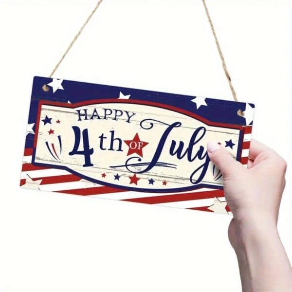 A hand holds adecorative wood plaques with stars and stripes that reads "Happy 4th of July.