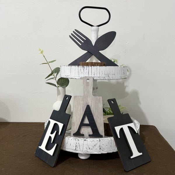 A two-tiered white tray with cutting boards spelling the EAT Letter Logo, decorative plants, and a Fork & Spoon Set crossed on top—perfect for cross-border wholesale kitchen decor.