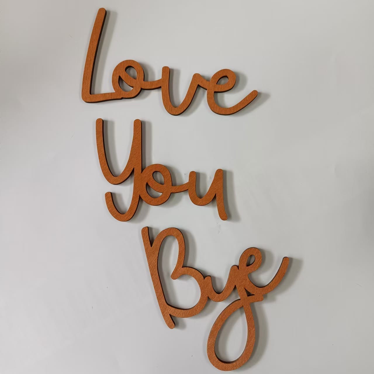 Wooden cutout letters arranged on a white surface spell out the phrase "Love You Bye" in cursive script, perfect as a charming wood wall decor or as part of a wholesale letter shape set.