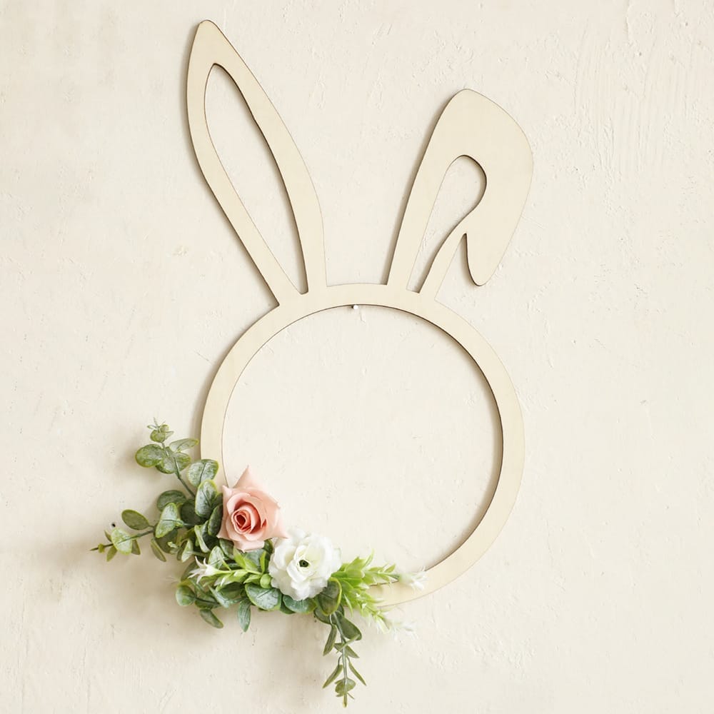 A minimalist bunny-shaped wreath, crafted as a Wooden Rabbit Shape with artificial greenery and pastel flowers, is mounted on a textured beige wall—perfect as a charming wood wall decoration.