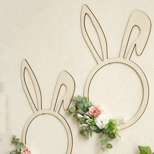 Two minimalist Wooden Rabbit Shape frames are mounted on a light wall, each decorated with artificial green leaves and pink and white flowers at the base—a charming wood wall decoration.
