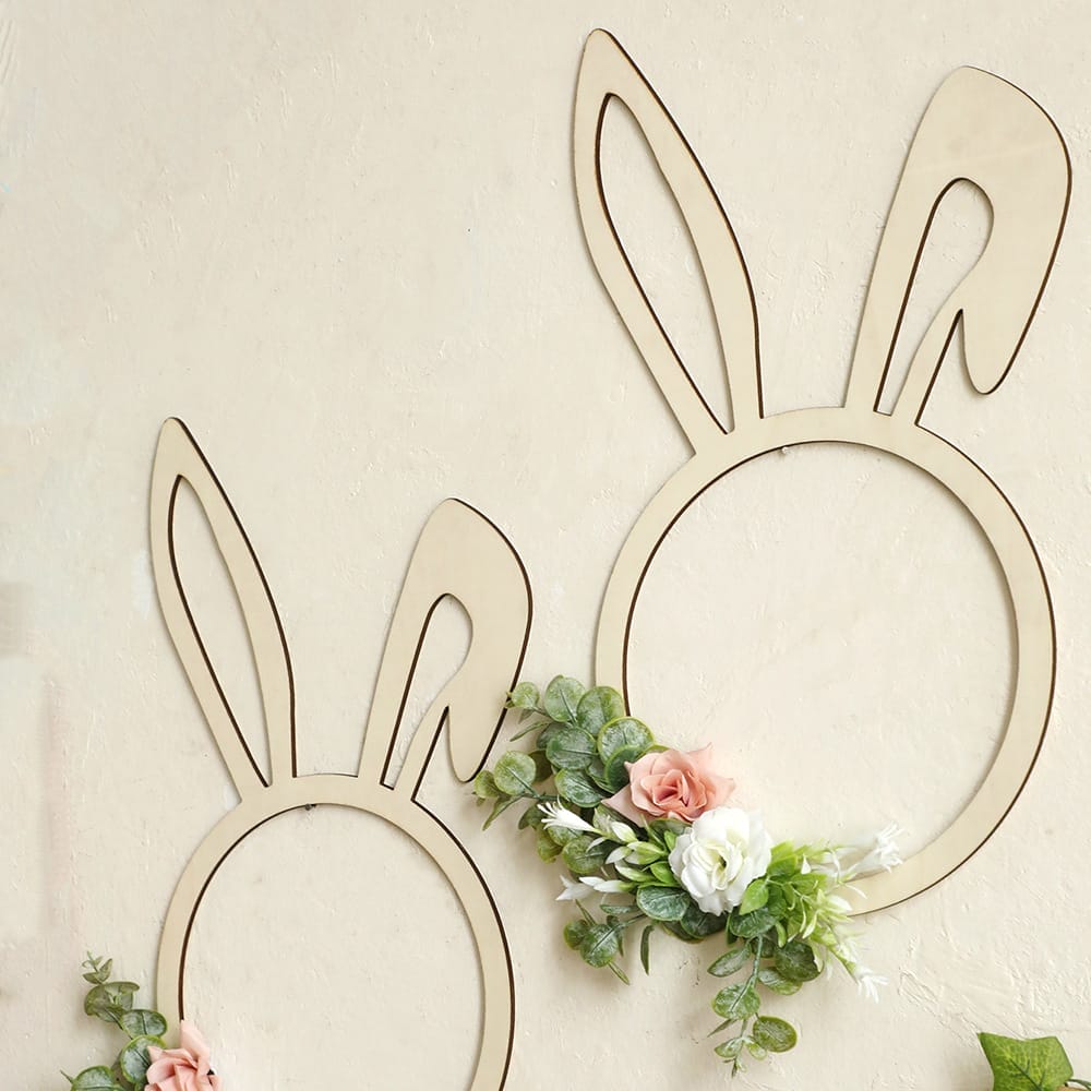 Two minimalist Wooden Rabbit Shape frames are mounted on a light wall, each decorated with artificial green leaves and pink and white flowers at the base—a charming wood wall decoration.