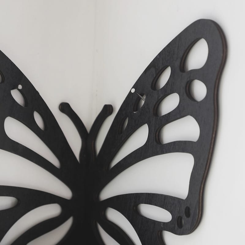 Close-up of a black, laser-cut wooden butterfly decoration mounted on a white wall, showing detailed cutout patterns on the wings.