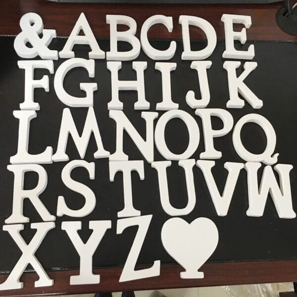White uppercase woodcut letters of the English alphabet and a heart shape are arranged in rows on a dark surface.