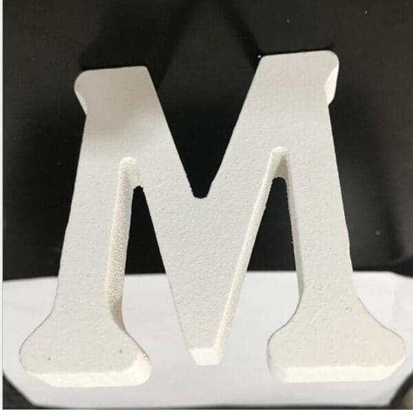 A white, three-dimensional letter "M" is placed on a black and white surface, making it a stylish choice for home decor.