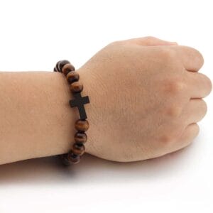 A hand wearing a wooden bead bracelet with a black cross charm on a white background.