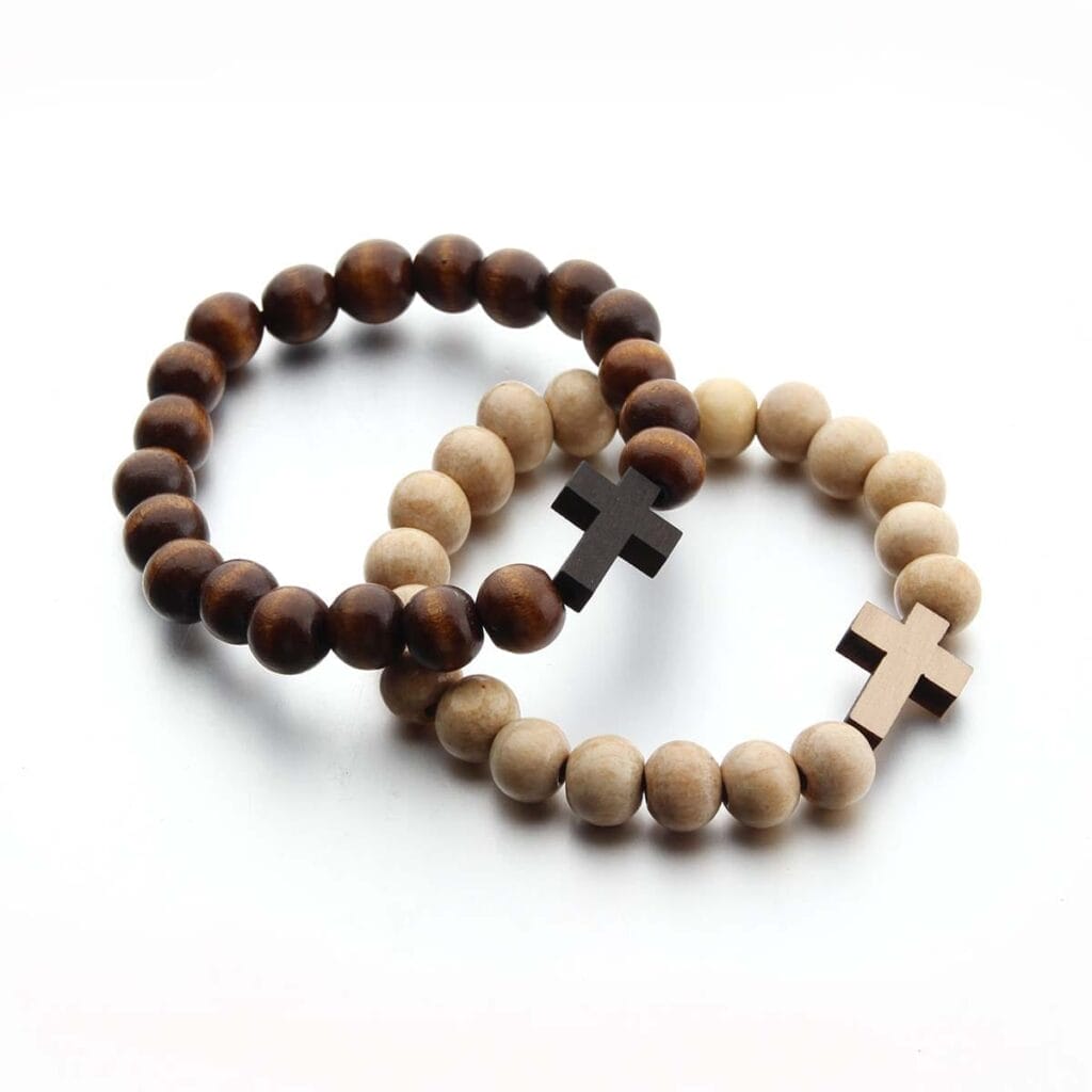 Two beaded bracelets, including a wooden bead bracelet with dark brown beads and a black cross, and another with light beige beads and a metallic cross, arranged overlapping on a white background.