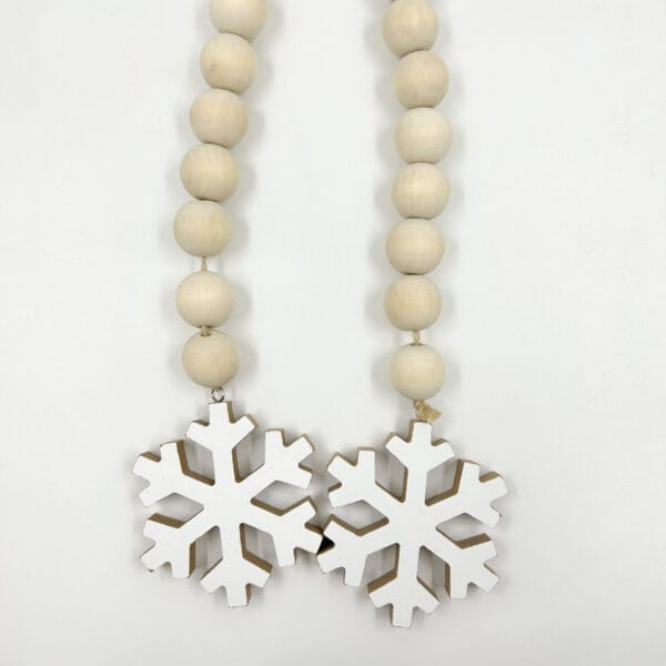 White wooden snowflake ornaments hang from a beige wooden bead garland. Wholesale wooden bead garland manufacturer.