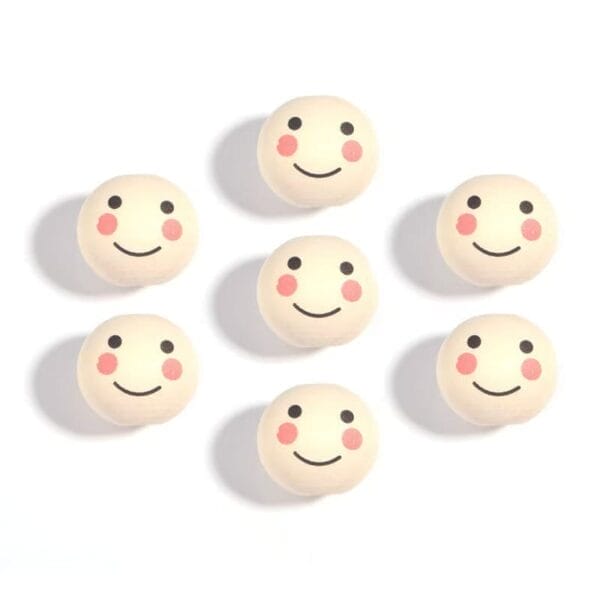 Seven round objects with simple smiling faces and pink cheeks are arranged on a white background.