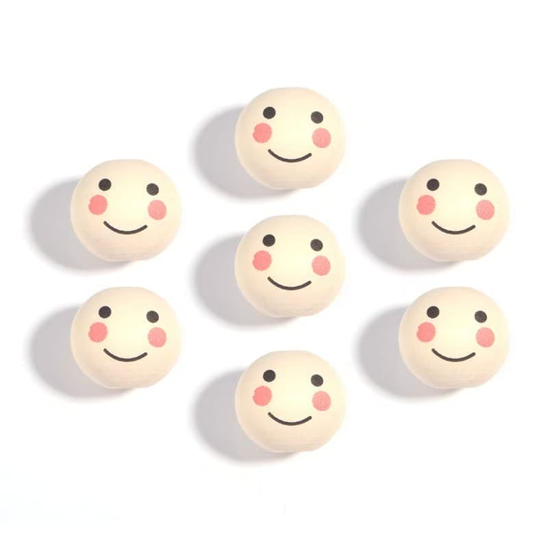 Seven round objects with simple smiling faces and pink cheeks are arranged on a white background.