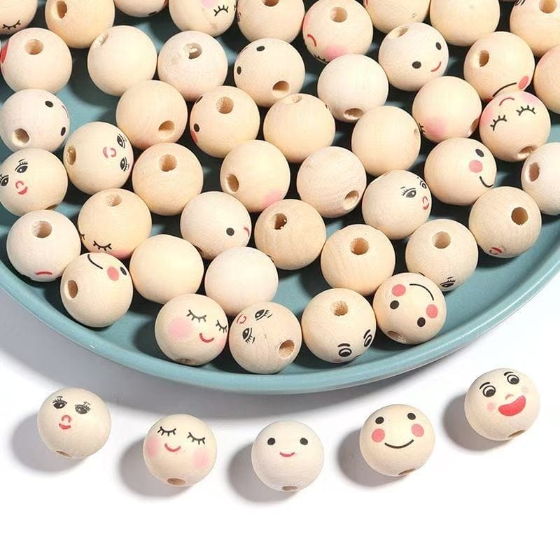 A blue plate filled with wooden beads, some featuring various hand-drawn facial expressions, with four additional decorated beads placed beside the plate.