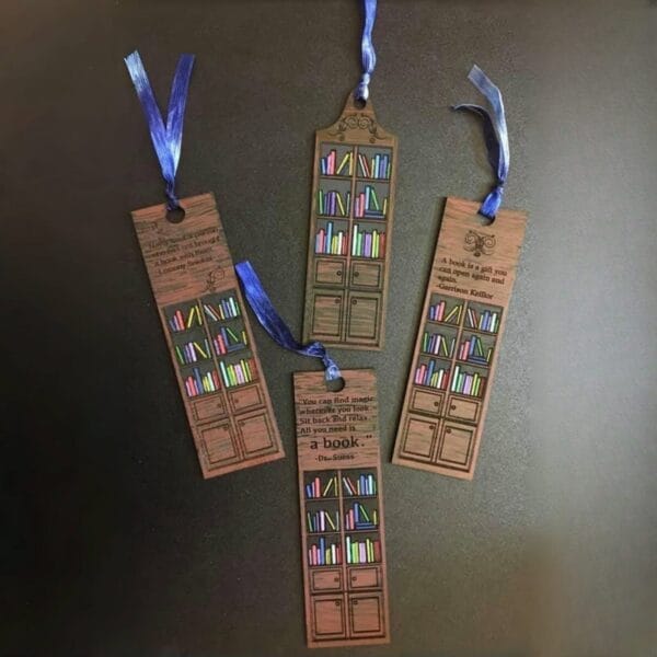 Four wooden bookmarks, crafted by a leading manufacturer, feature bookshelf designs and blue ribbons. Each wooden bookmark displays colorful books and engraved quotes, arranged beautifully on a black surface.