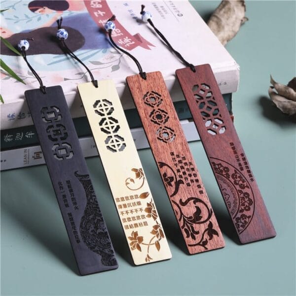 Four intricately carved wooden bookmarks with tassels are displayed on top of stacked books, each featuring unique designs and engraved text that highlight the natural beauty of wooden bookmarks.