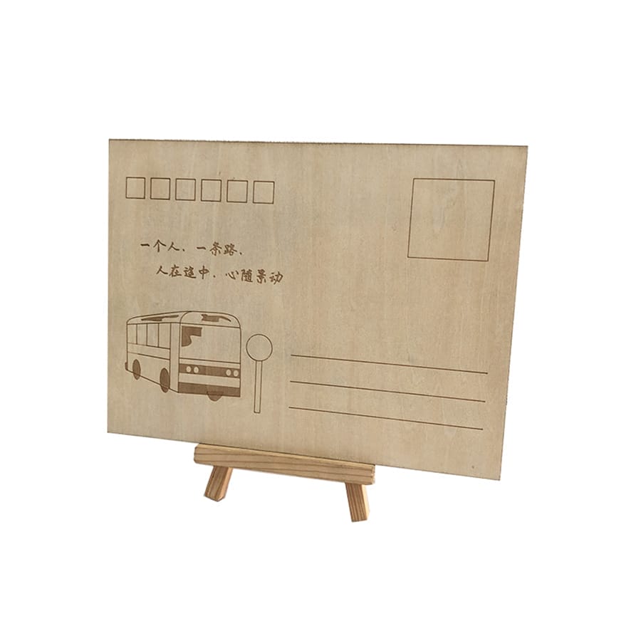 A wooden business card postcard on a small easel features an engraved bus, bus stop, and lines for address and stamp. Chinese text is also beautifully engraved on the card.