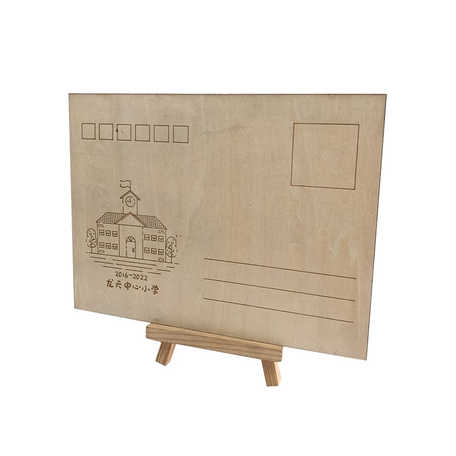 A wooden plaque shaped like a postcard, engraved with a school building, dates, and address lines—like a unique wooden business card—displayed on a small wooden easel.