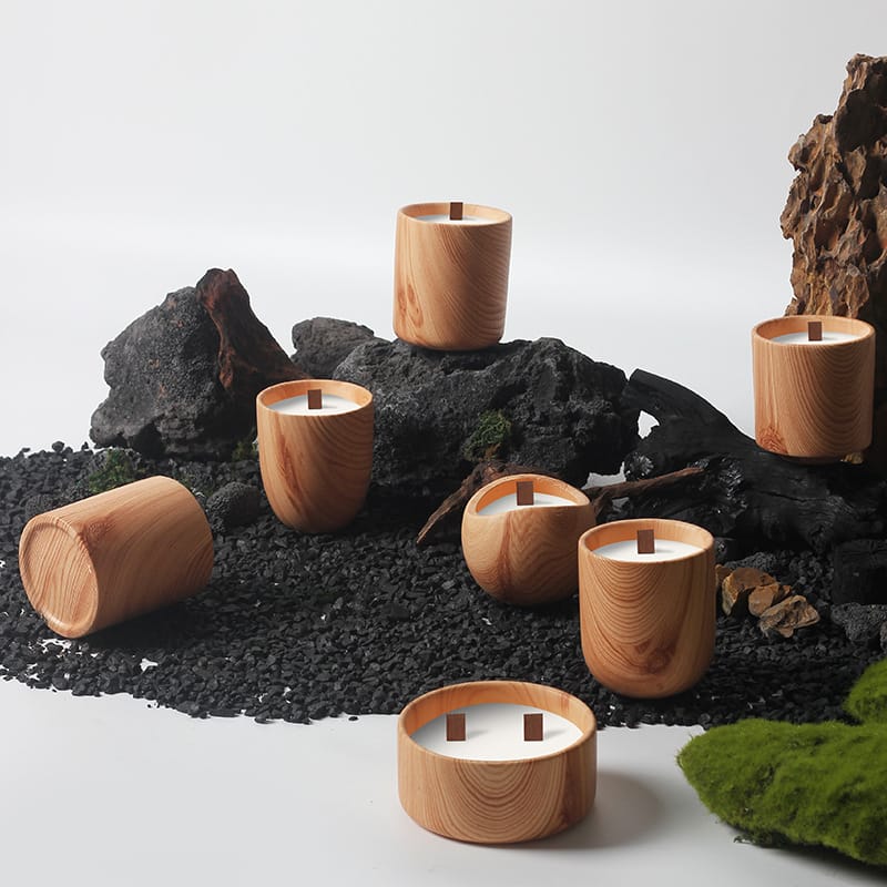 Wooden candle holder with open tops and square center handles are arranged on black gravel and rocks, accented by moss, against a plain white background.