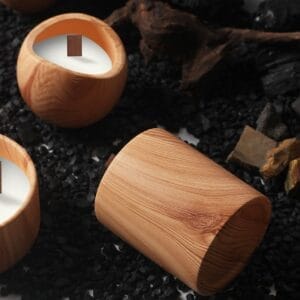 Round wooden candles with wooden wicks sit atop black stones, surrounded by dark wood pieces and rocks—a serene display inspired by a Nordic minimalist candle holder aesthetic.