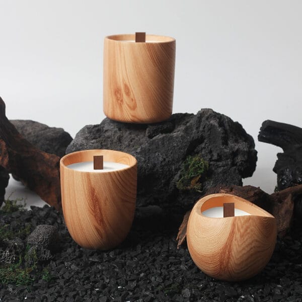 Three wooden candles with visible wood grain and wooden wicks are arranged on black rocks and surrounded by driftwood and moss, capturing the charm of a Nordic minimalist candle holder design.