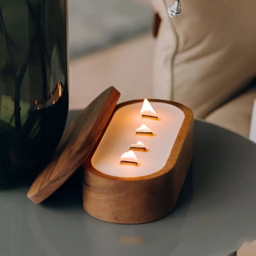 A wooden candle holder with a partially open lid reveals four lit triangular candles arranged in a row on a white base, placed on a round glass table—an elegant touch for refined restaurant ambiance.