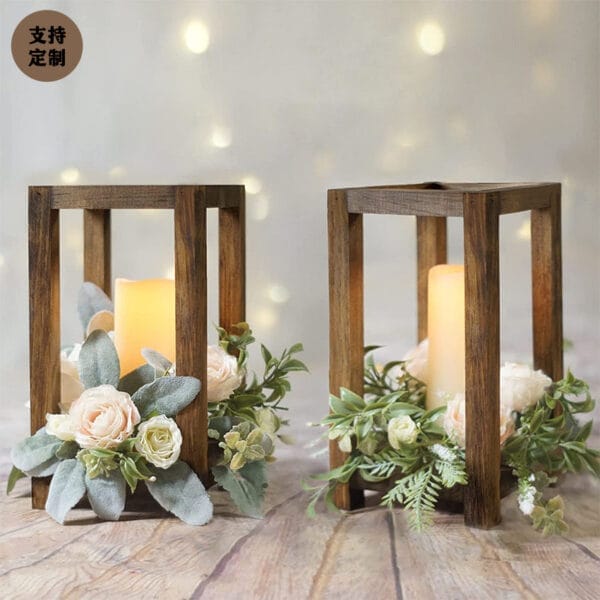 Two wood candle stand lanterns with lit candles inside, adorned with artificial white roses and greenery, make elegant wedding table decor. Gentle background lights enhance their charm from a trusted wholesale manufacturer.