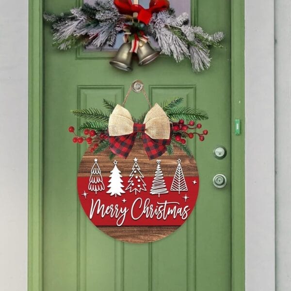 A green door adorned with Rustic Holiday Decor: a wreath of bells and frosted branches above, plus a round "Merry Christmas" sign with trees, berries, and a bow—perfect for welcoming guests to any holiday party.