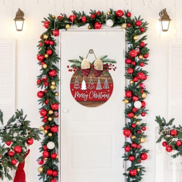 A white door decorated with a "Merry Christmas" sign and surrounded by rustic holiday decor, including garlands of red and gold ornaments; small trees and a wooden Christmas wreath complete the festive scene.