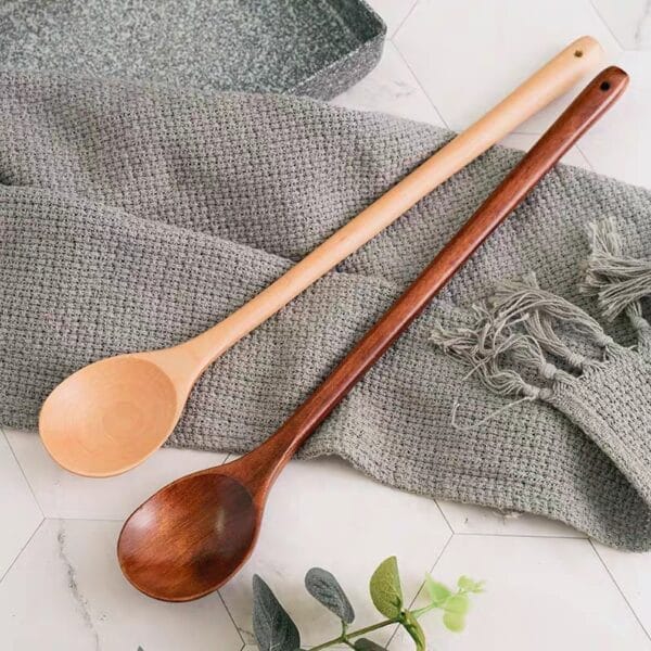 Two wooden cooking spoon, one light and one dark, rest on a gray textile. Wholesale wooden spoons.