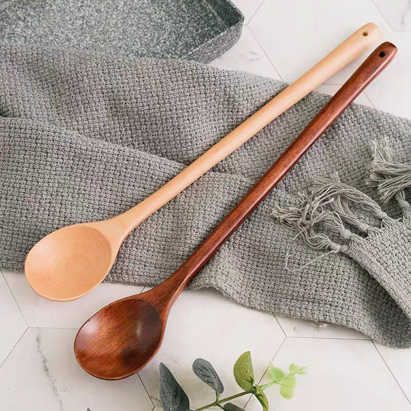 Two wooden cooking spoon, one light and one dark, rest on a gray textile. Wholesale wooden spoons.