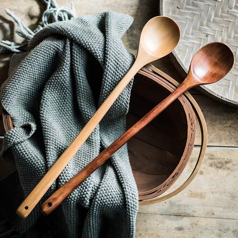 Two long wooden cooking spoons rest on a gray knitted blanket. Wholesale wooden cooking spoon manufacturer.