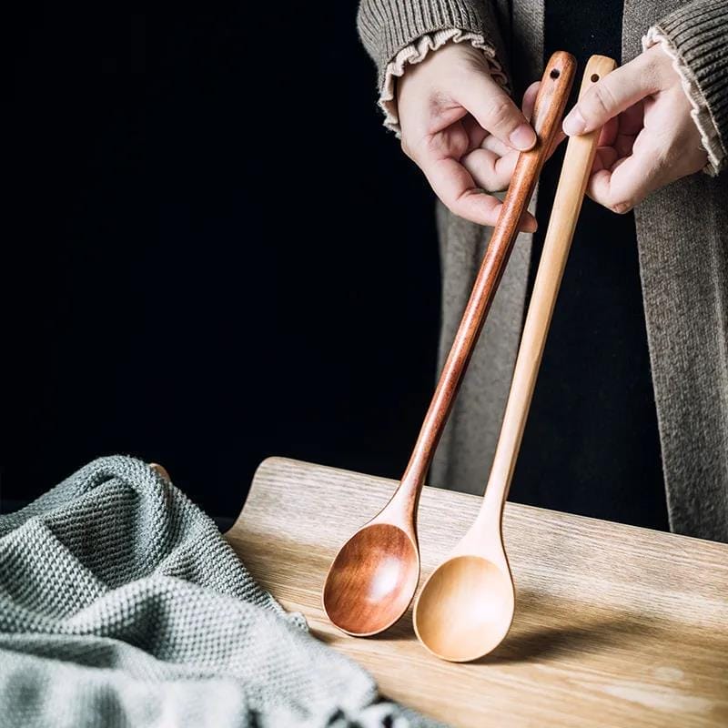 Hands holding two long wooden cooking spoons, one dark and one light. Wholesale wooden spoon supplier.