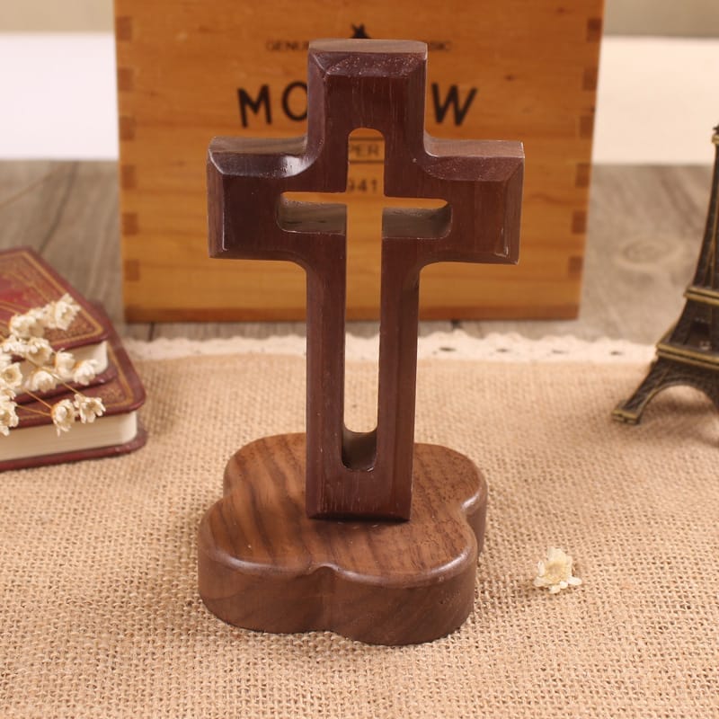 A wooden cross on a clover-shaped base sits on a burlap mat, with a book, box, and small Eiffel Tower figurine in the background, highlighting the rustic charm of the wooden cross.