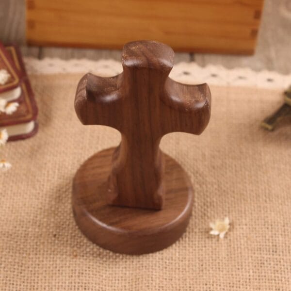 A wooden cross on a round wooden base sits on burlap, beside a book and scattered flower petals—an inspiring DIY decorative craft perfect for home decor or global distributors.