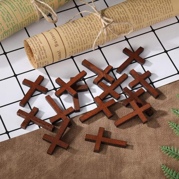 Several small wooden cross pendants are scattered on a brown surface next to a rolled sheet of printed paper, with a white tiled background partially visible.