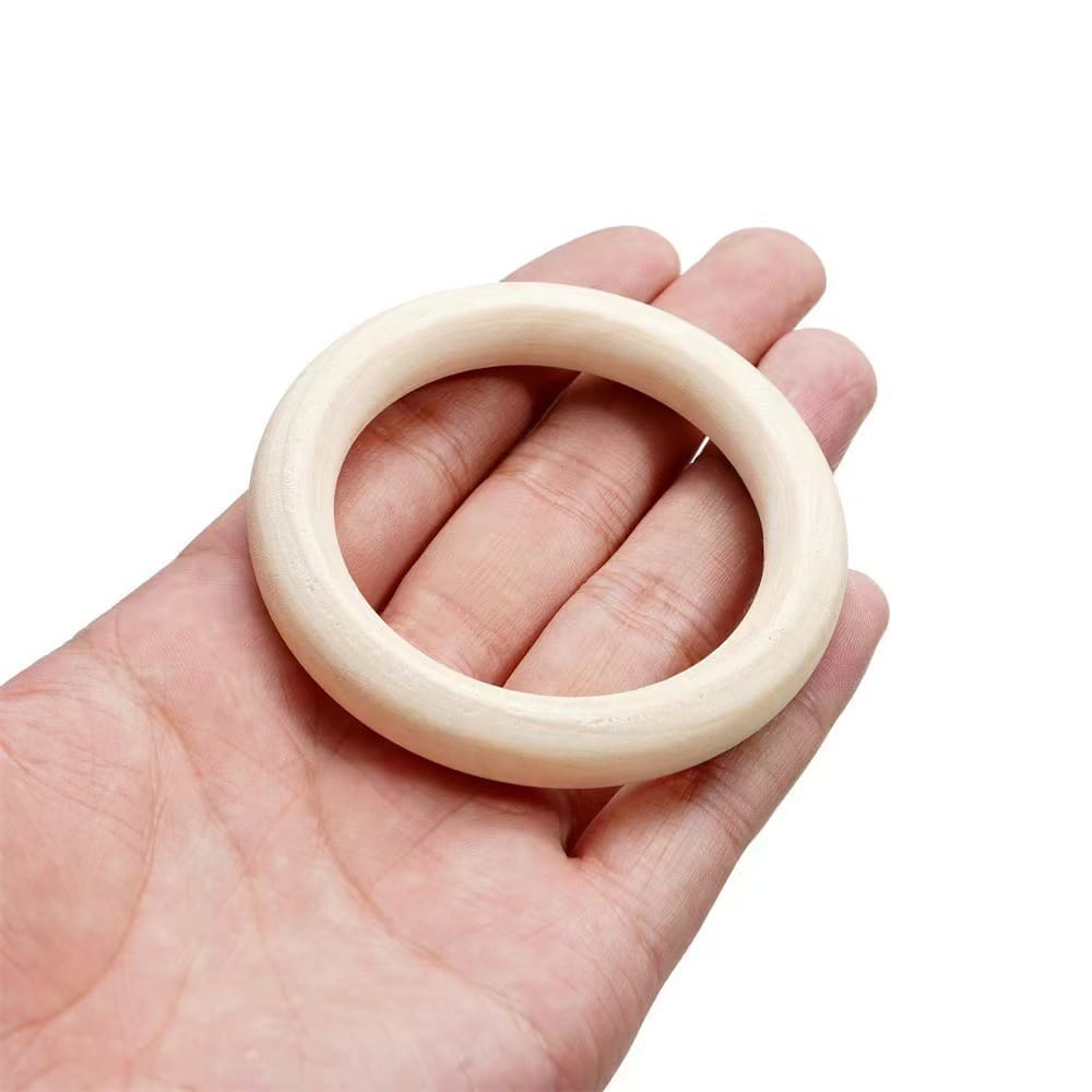 A hand holding a smooth, round, light-colored wooden curtain ring against a plain white background.