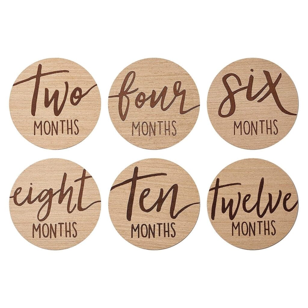Six round wooden discs feature milestone plaques labeled with "two months," "four months," "six months," "eight months," "ten months," and "twelve months" in elegant cursive writing.
