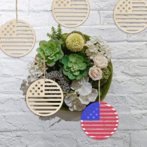 A wreath of green succulents and white flowers hangs on a white brick wall, surrounded by five wooden American flag ornaments—a festive American Independence Day decoration—one painted in red, white, and blue.