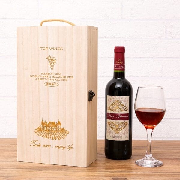 A bottle of red wine, a filled wine glass, and a wooden gift box with engraved text and illustrations are displayed on a wooden surface against a white background.