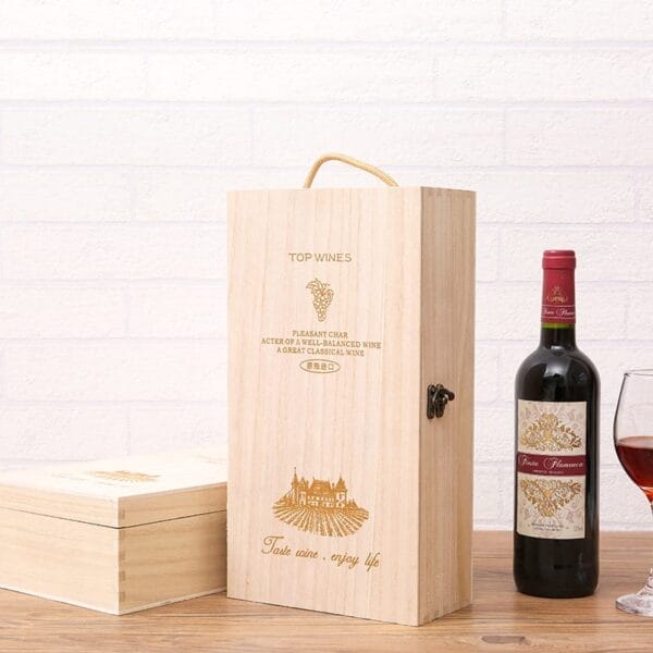 A custom wooden wine box stands next to a bottle of red wine and a glass, all set on a wooden surface against a white brick wall.