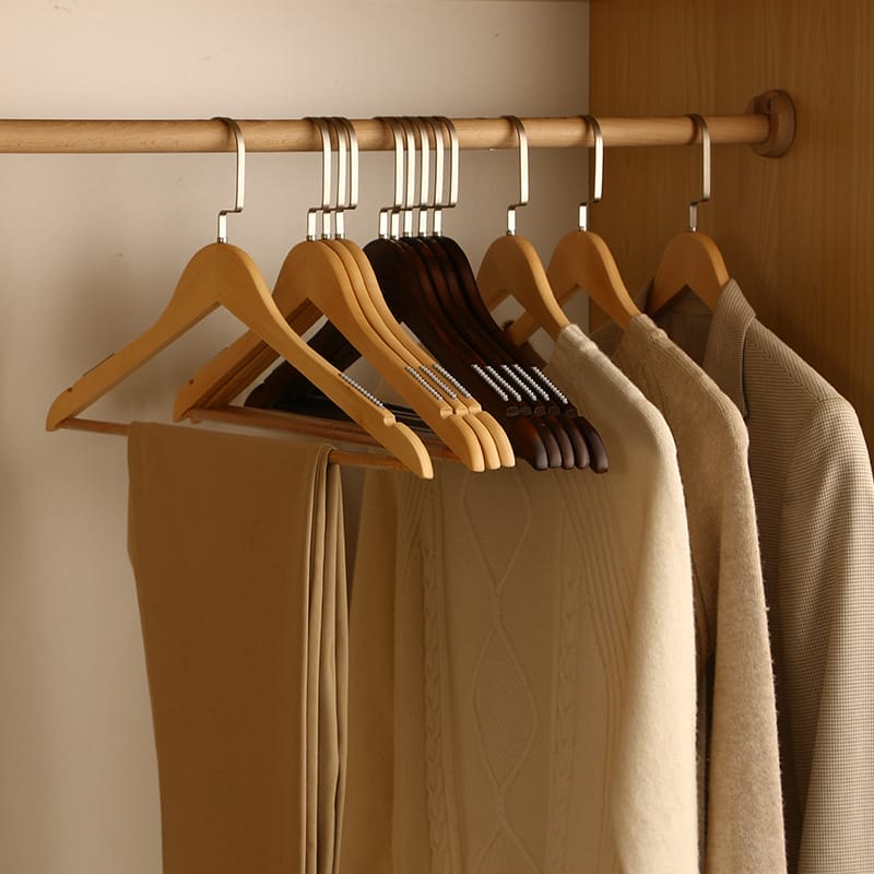 A row of wooden hangers holding beige and brown clothing items, including sweaters, pants, and jackets, hanging on a wooden closet rod.