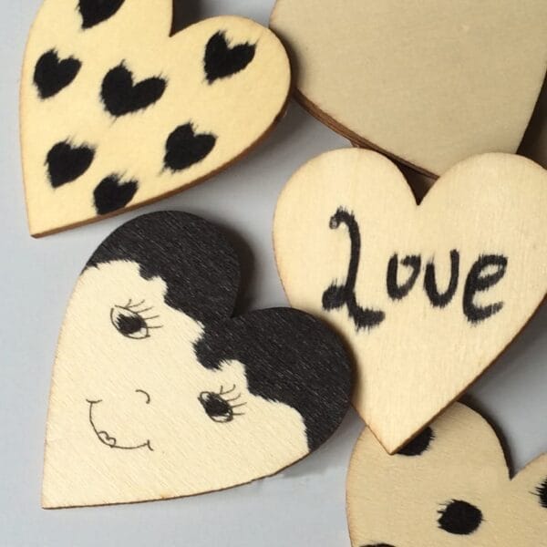 Several hand-painted wooden heart-shaped pieces are adorned with black markings, including polka dots, the word "Love," and a smiling face—perfect as craft decorations.