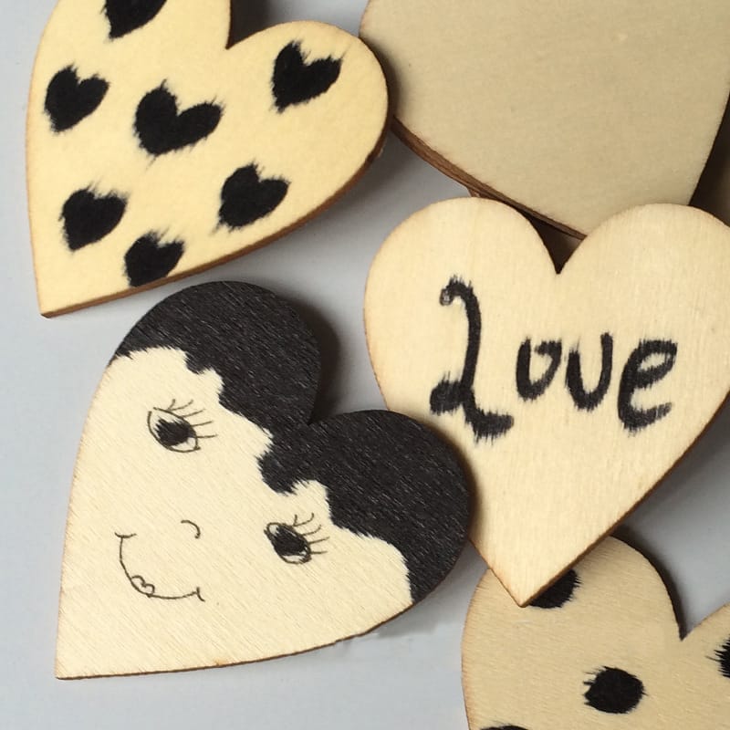 Several hand-painted wooden heart-shaped pieces are adorned with black markings, including polka dots, the word "Love," and a smiling face—perfect as craft decorations.
