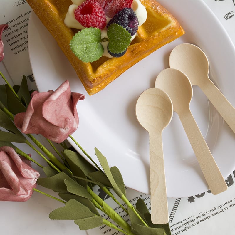 Wooden ice cream spoons on a plate with waffles and berries. Eco-friendly wholesale spoons.