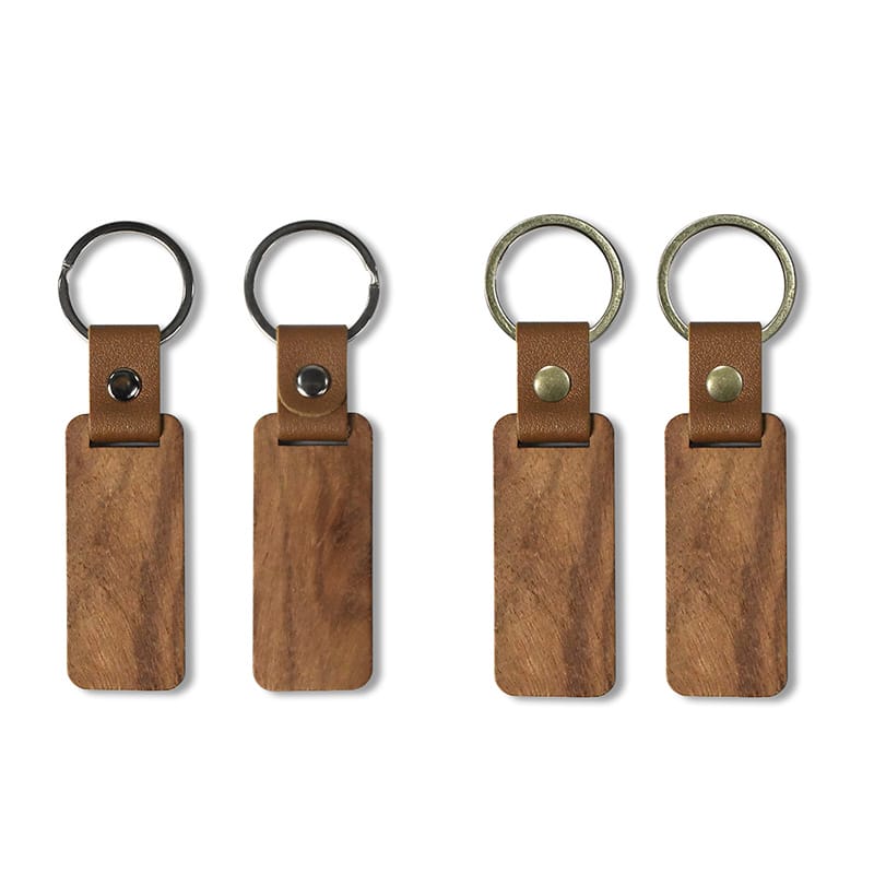 Four rectangular wooden keychains with leather straps and metal rings are arranged in a row. The two wooden keychains on the left feature silver rings, while those on the right display brass rings.