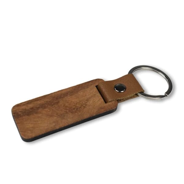 A rectangular wooden keychain with a metal keyring and a brown leather strap attached by a metal rivet, ideal for those seeking custom laser-cut keychains with timeless style.